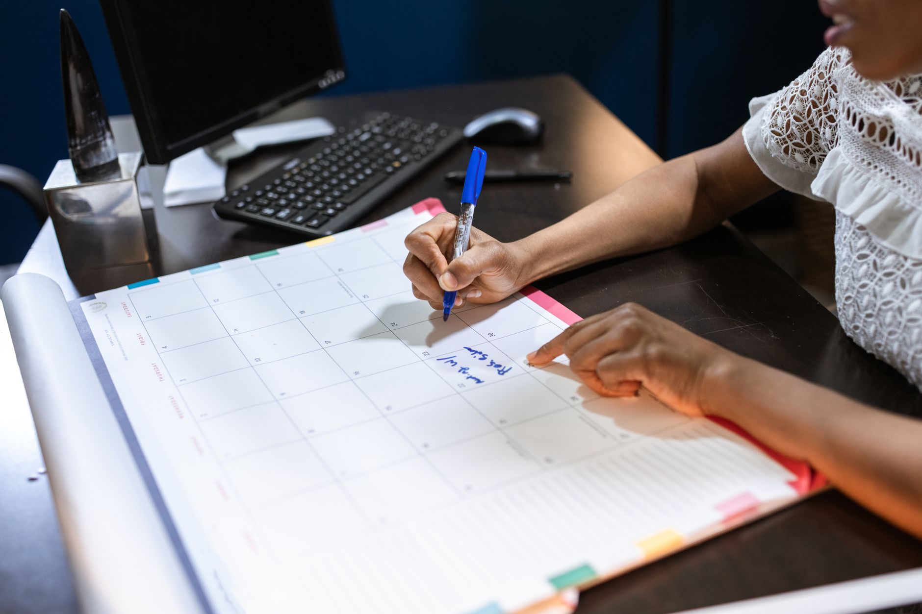 Persona organizando tareas de trabajo en un calendario junto a su computadora